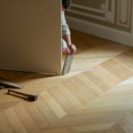 Artisan en train de raccorder un parquet ancien en chêne à l'emplacement d'une cloison abattue dans un appartement haussmannien